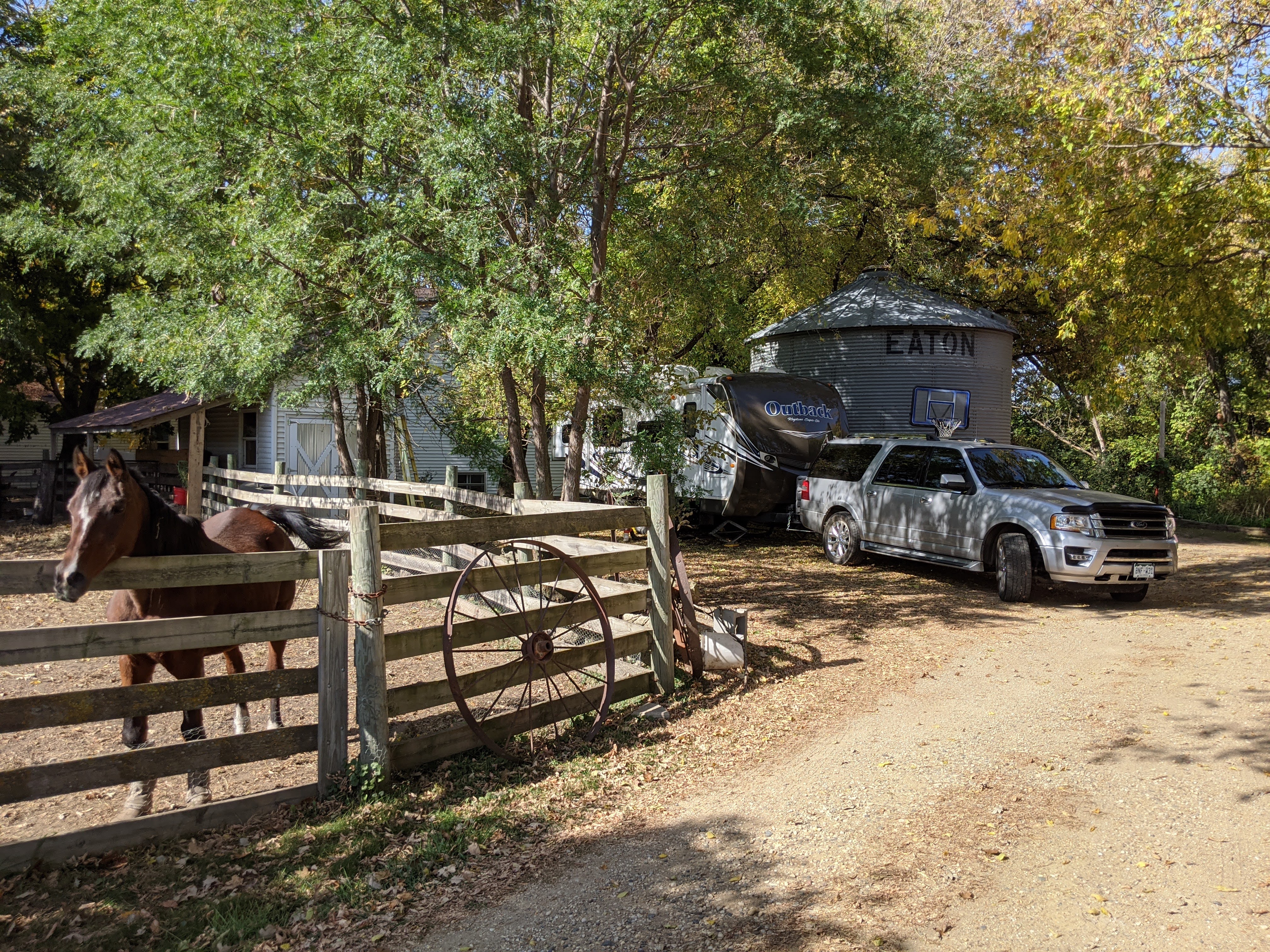 rig parked under trees, between fenced horse in foreground and small silo